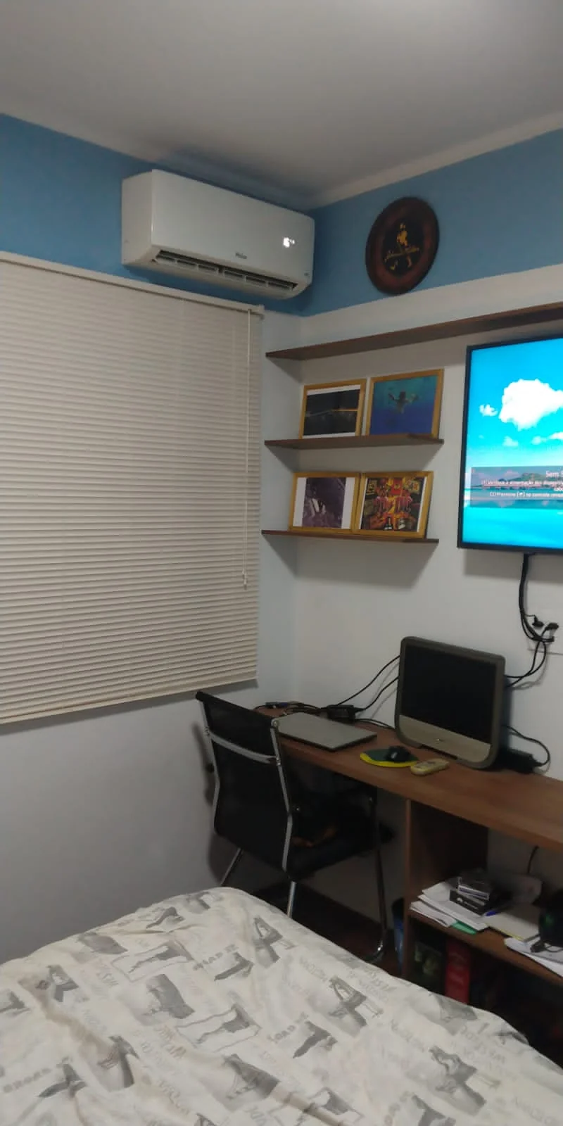 Home office em quarto pequeno com bancada de madeira, prateleiras com vinis emoldurados e parede azul petróleo, Limeira — DOA Estúdio
